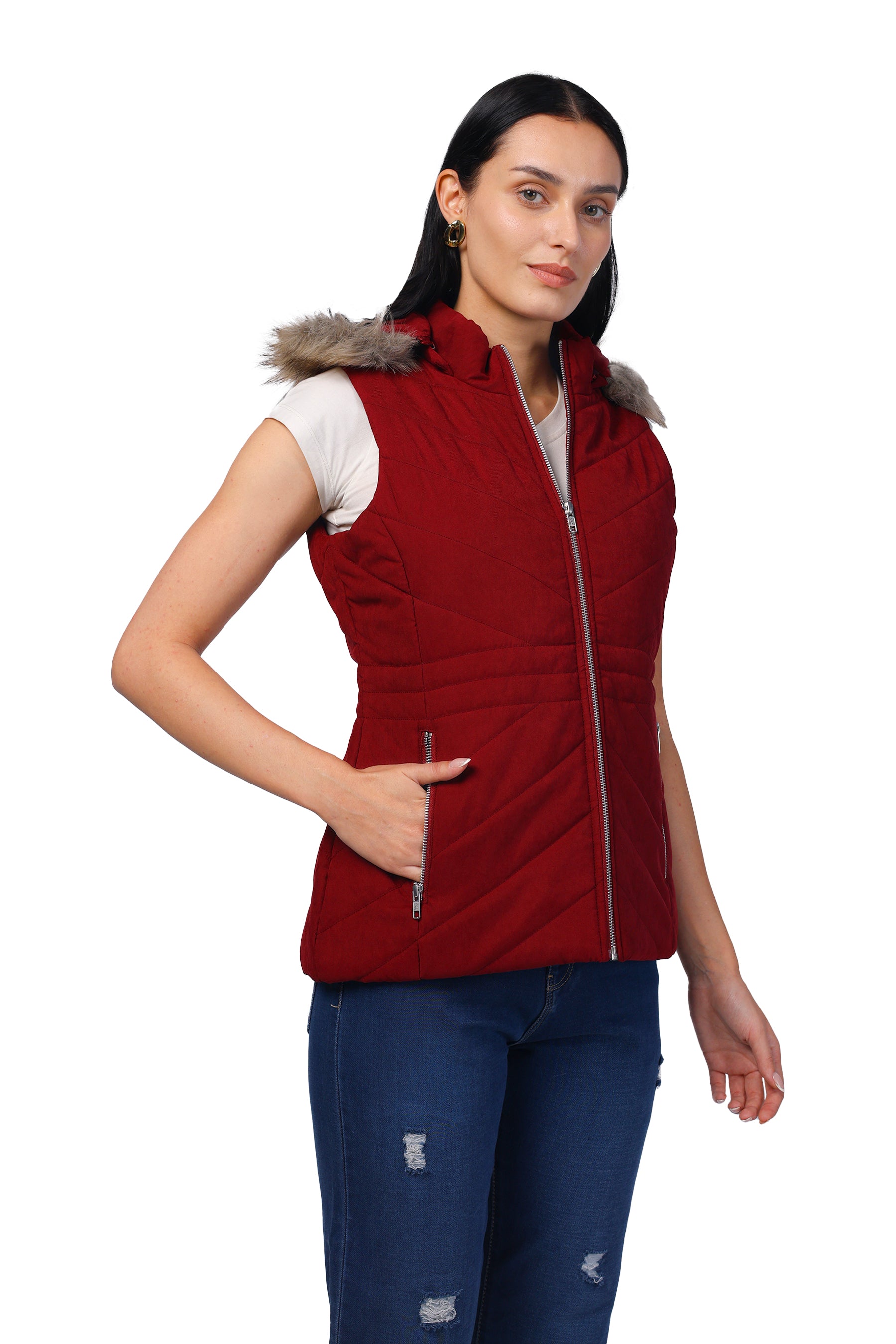 A woman modeling a sleeveless red puffer vest with a faux-fur trimmed hood and front zipper, paired with blue jeans, against a plain white background.