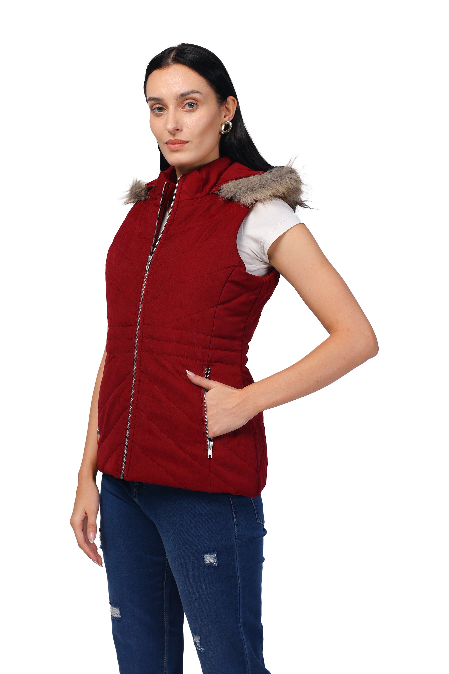 A woman modeling a sleeveless burgundy puffer vest with a gray faux-fur trimmed hood, worn over a white t-shirt and blue jeans, against a plain white background.