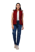 A woman modeling a sleeveless burgundy puffer vest with a faux-fur trimmed hood, worn over a white t-shirt and blue jeans, against a plain white background.
