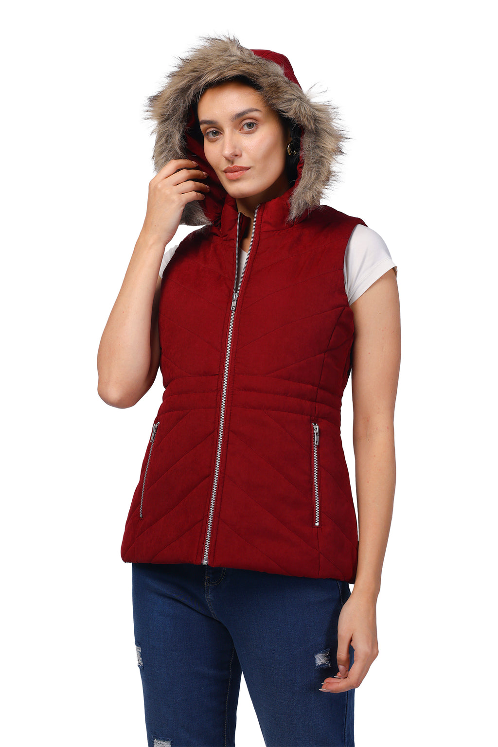A woman wearing a sleeveless quilted red puffer vest with a faux-fur trimmed hood, silver zippers, and a white t-shirt underneath, paired with blue jeans against a white background.