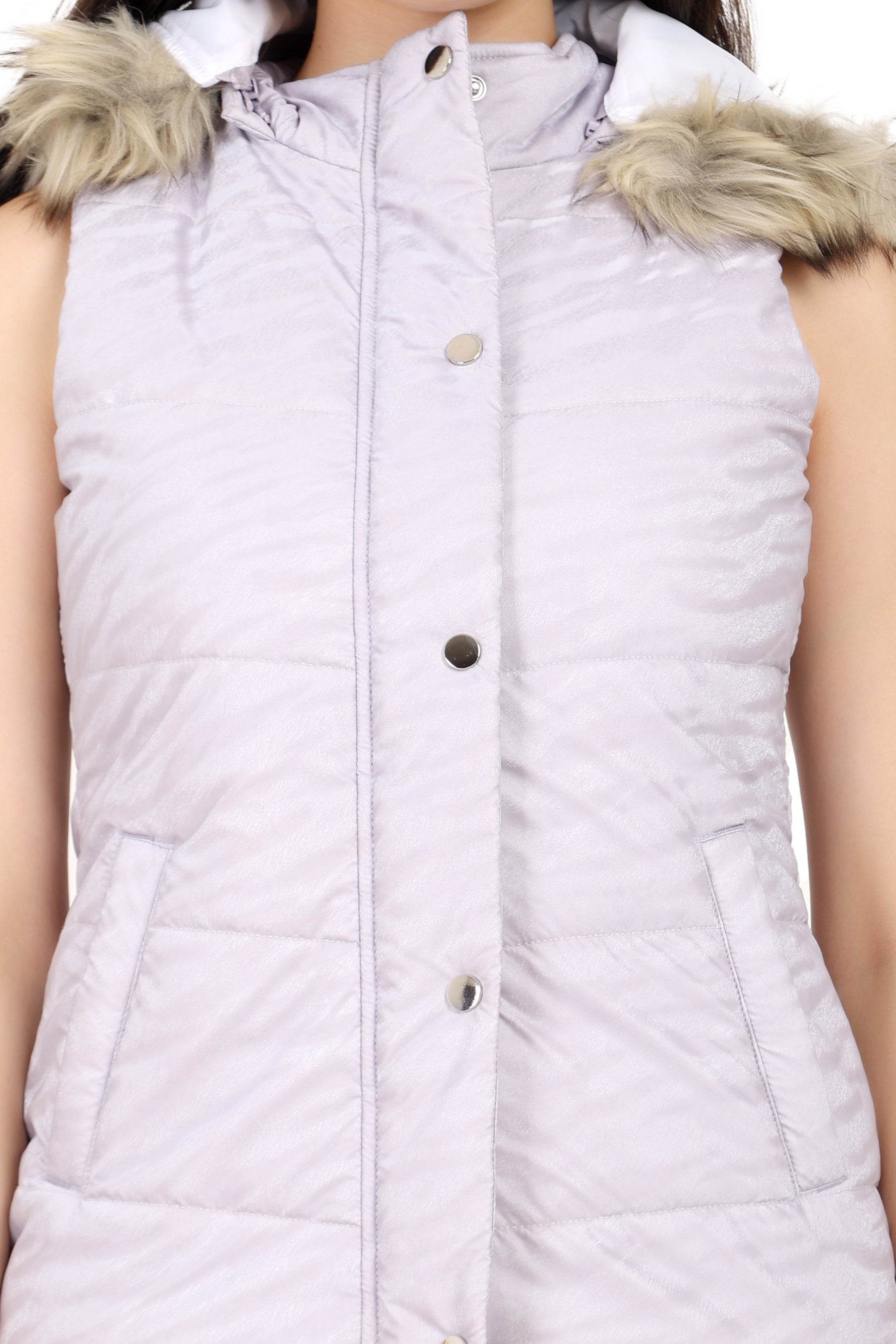 A close-up of a sleeveless quilted puffer vest in a very light lavender or pale lilac color, featuring a faux fur-trimmed hood and front snap buttons.