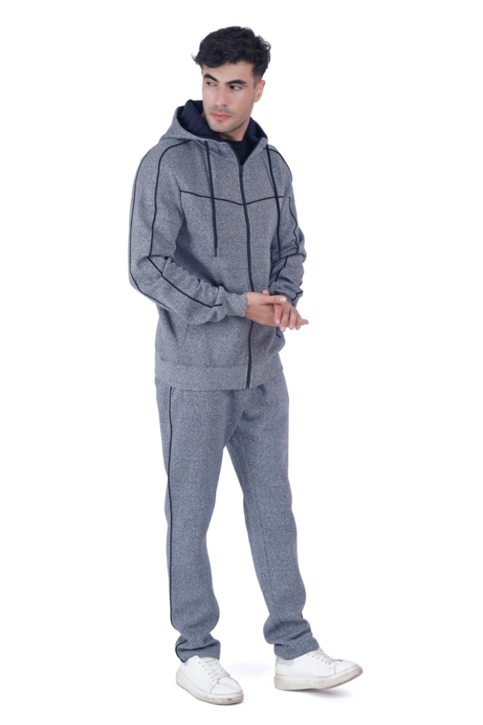 A man in a Coatsmore’s navy hooded tracksuit with black piping, standing in a relaxed pose and looking to the side, wearing white sneakers, against a white background.