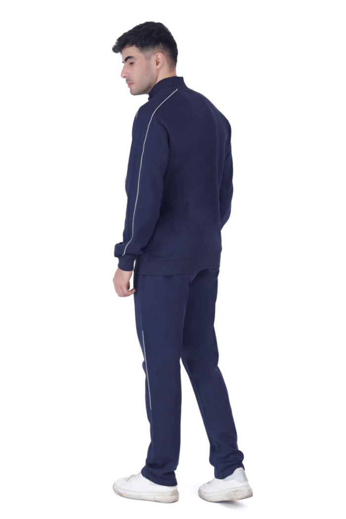 A man in coatsnmore’s navy blue tracksuit with white piping, shown from the back while turning his head slightly to the side, wearing white sneakers against a plain white background.