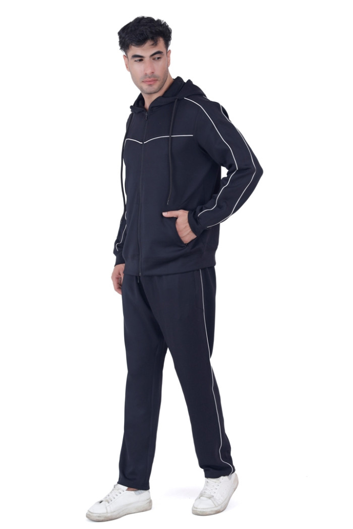 A man in Turfit’s black hooded tracksuit featuring white piping details, posing casually with one hand in the pocket and head turned slightly, wearing white sneakers against a plain white background.