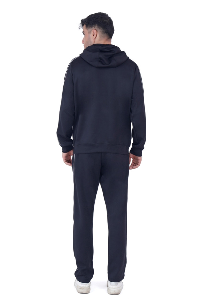 A man wearing Turfit’s black hooded tracksuit with white piping, shown from the back while standing straight, paired with white sneakers against a plain white background.