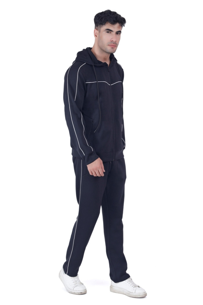 A man in Turfit’s black hooded tracksuit with white piping, walking forward in a casual pose while looking ahead, paired with white sneakers against a white background