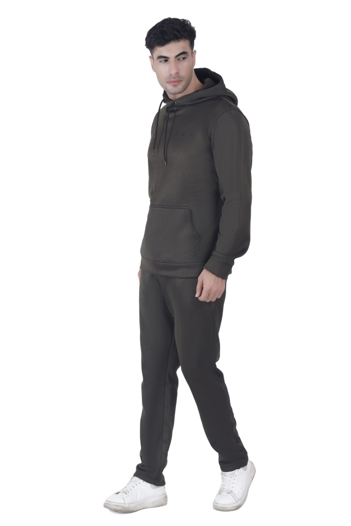 A man in Coatsnmore’s olive hooded tracksuit with a front pouch pocket and drawstring hood, posing in a side-facing stance with relaxed hands, wearing white sneakers against a white background.