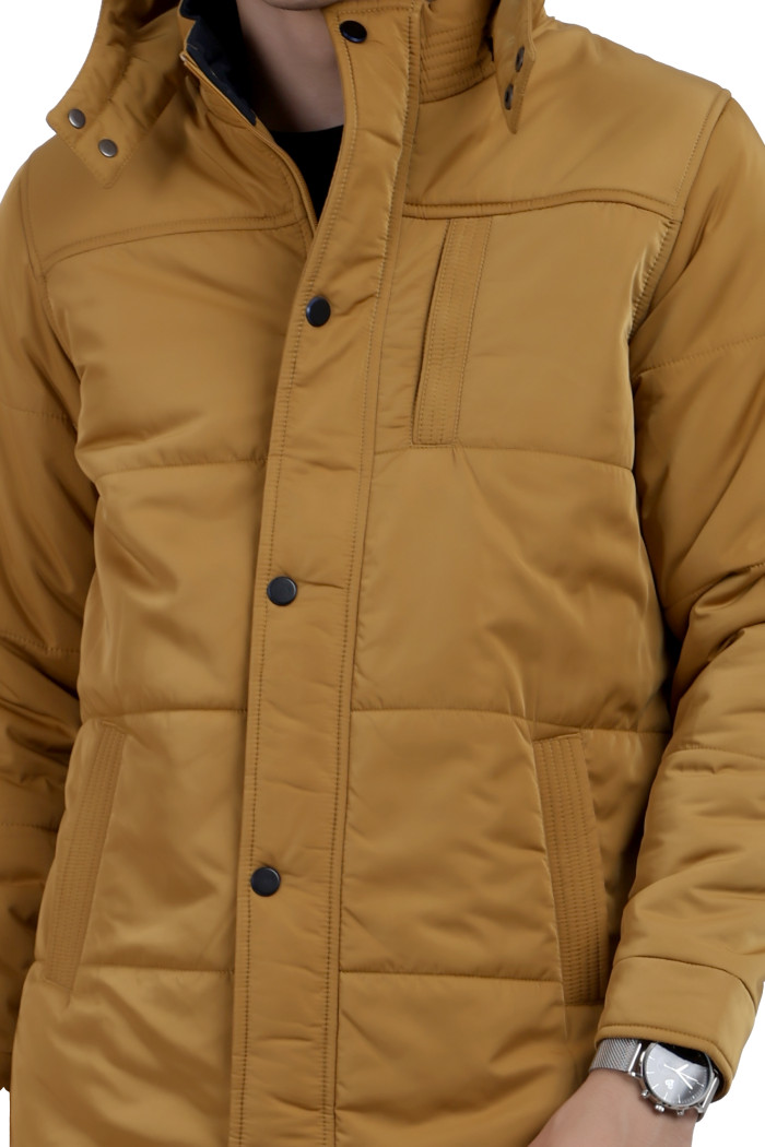 A cropped image of a man wearing a Mustard quilted jacket with a high neck collar, hood , zipper closure and pocket in hand designed for casual winter layering and comfort.