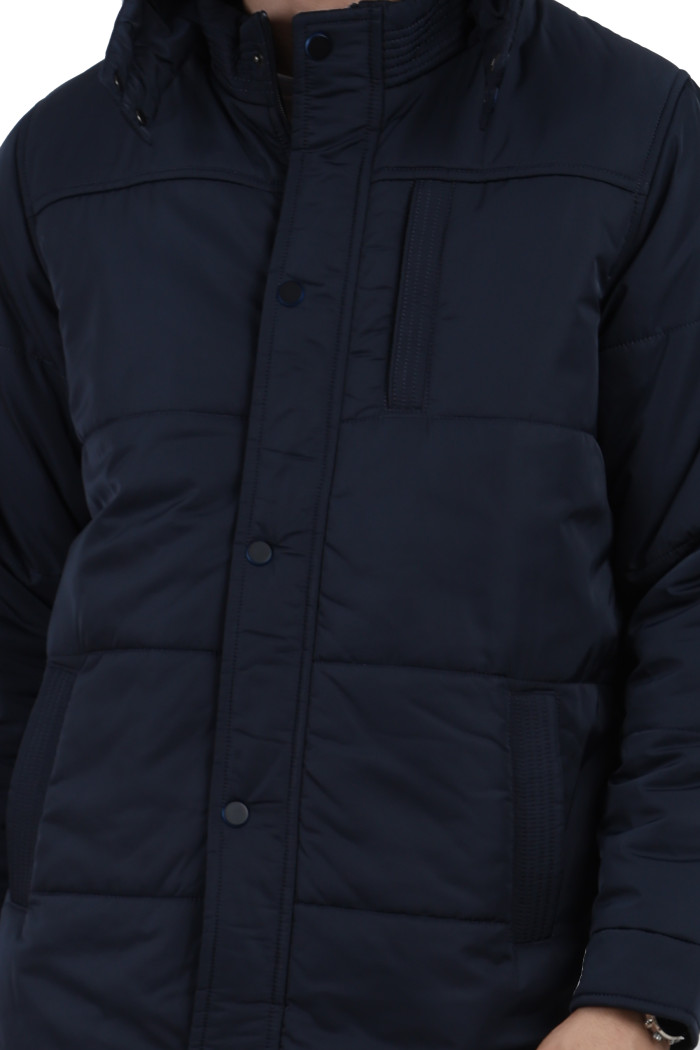 A cropped image of a man wearing a Navy quilted jacket with a high neck collar, hood , zipper closure and pocket in hand designed for casual winter layering and comfort.