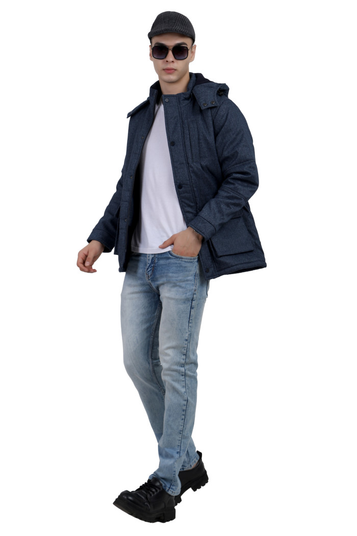 A tilted pose of a man wearing a Navy Chester jacket with a high neck collar, hood , zipper closure and pocket in hand designed for casual winter layering and comfort.