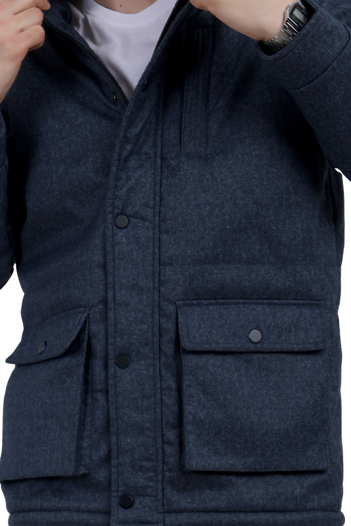 A cropped image of a man wearing a Navy Chester jacket with a high neck collar, hood, zipper closure, and pocket in hand designed for casual winter layering and comfort.