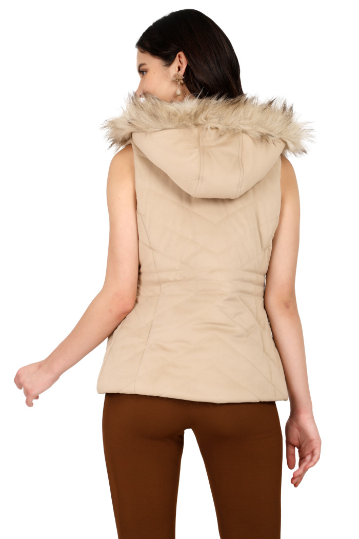 A back pose of a standing woman, wearing Coatsnmore’s half sleeves jacket in beige colour with a textured pattern, removable hood with faux fur trim, and coffee jeans.