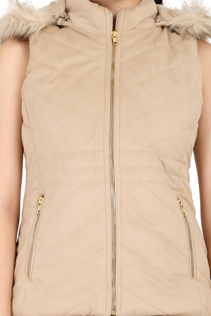 A cropped shot of a woman wearing Coatsnmore’s half sleeves jacket in beige colour with a textured pattern, removable hood with faux fur trim, side zippered pockets and a zip closure.