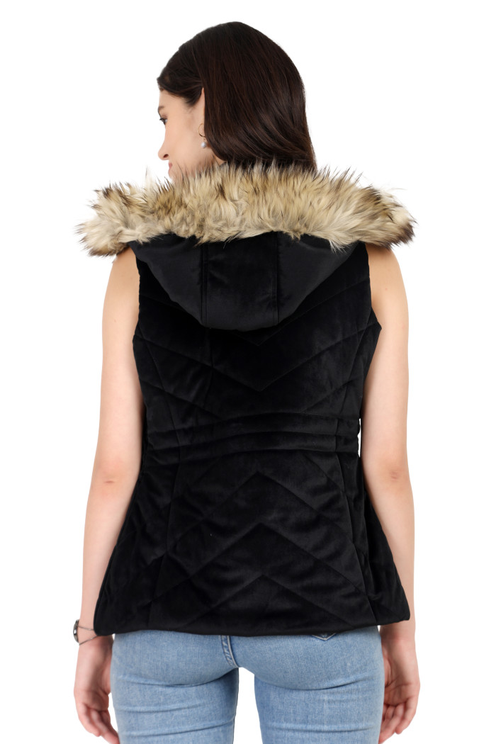 A back pose of a standing woman, wearing Coatsnmore’s half sleeves jacket in black colour with a textured pattern, removable hood with faux fur trim, and blue jeans.