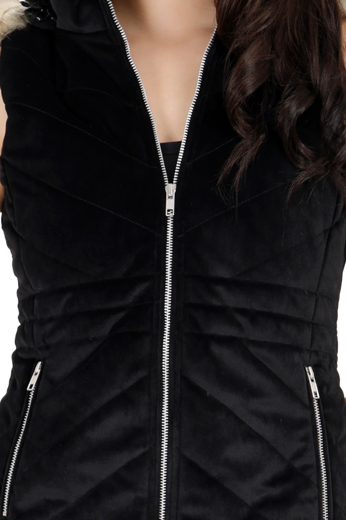 A cropped shot of a woman wearing Coatsnmore’s half sleeves jacket in black colour with a textured pattern, removable hood with faux fur trim, side zippered pockets and a zip closure.