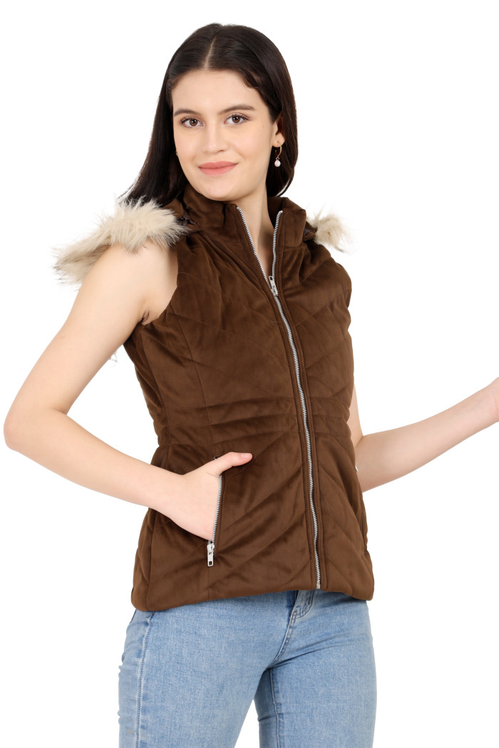 A standing side pose of a woman wearing Coatsnmore’s half sleeves jacket in blue colour with a textured pattern, removable hood with faux fur trim, side zippered pockets, a zip closure and black jeans while holding her fingers.