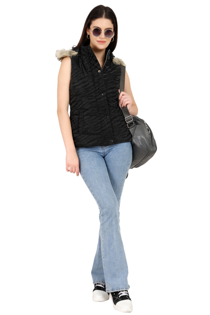 A woman in a standing pose in black shades, wearing Coatsnmore’s black quilted jacket with a high neck, zip closure, removable hood with faux fur trim, button plackets, and blue jeans, holding a bag from her left hand.