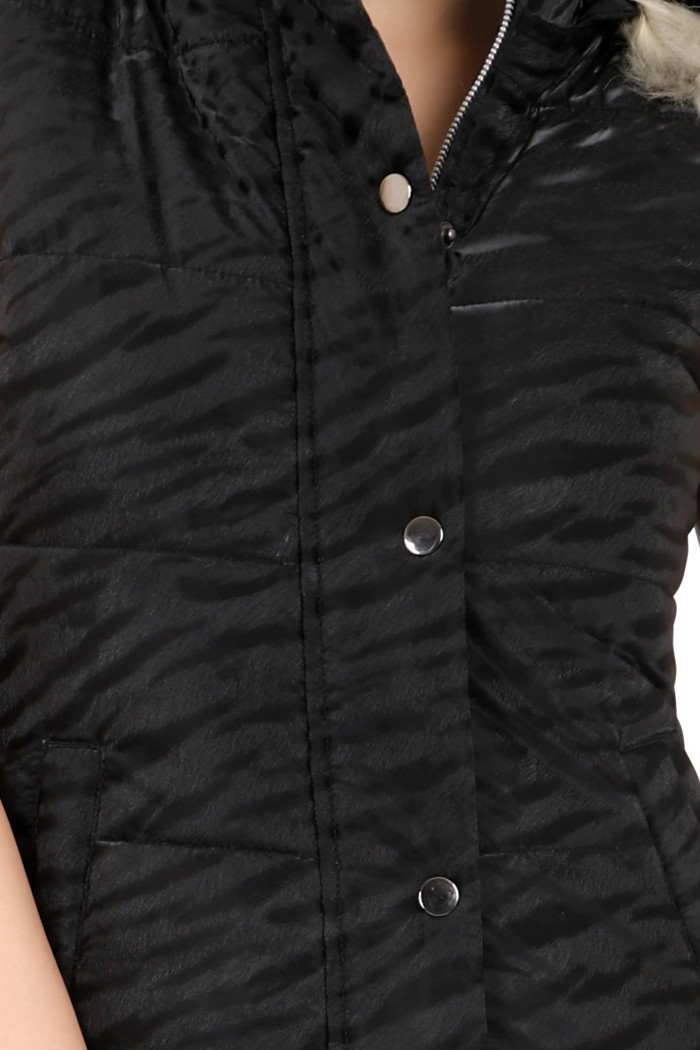 A woman in a cropped image is wearing Coatsnmore’s black sleeveless quilted jacket with a zip closure and button plackets.