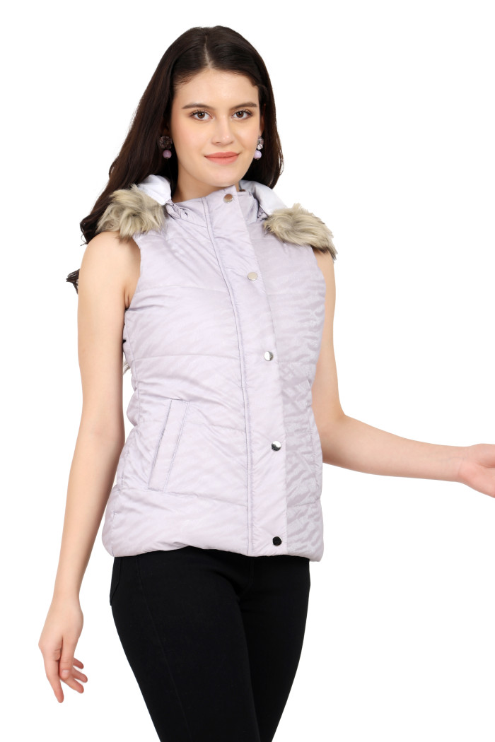 A standing pose of a woman wearing Coatsnmore’s lilac sleeveless quilted jacket with a zip closure, mandarin collar, removable hood, button plackets and black jeans.