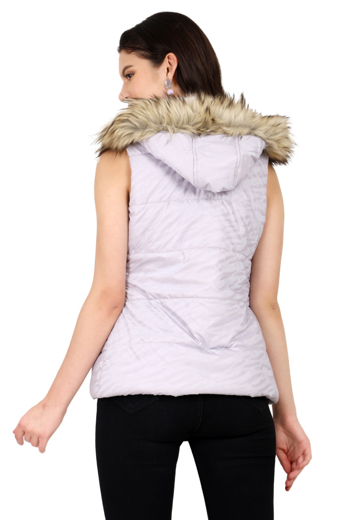 A back pose of a standing woman, wearing Coatsnmore’s lilac sleeveless quilted jacket with a mandarin collar and removable hood and black jeans.