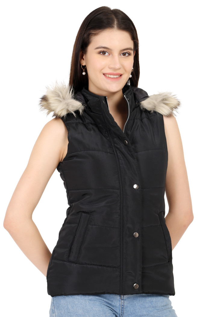 A woman in a standing side pose, wearing Trufit’s black half-sleeve quilted jacket with button placket, zip closure, side pockets, a removable hood and blue jeans with her hands at the back.