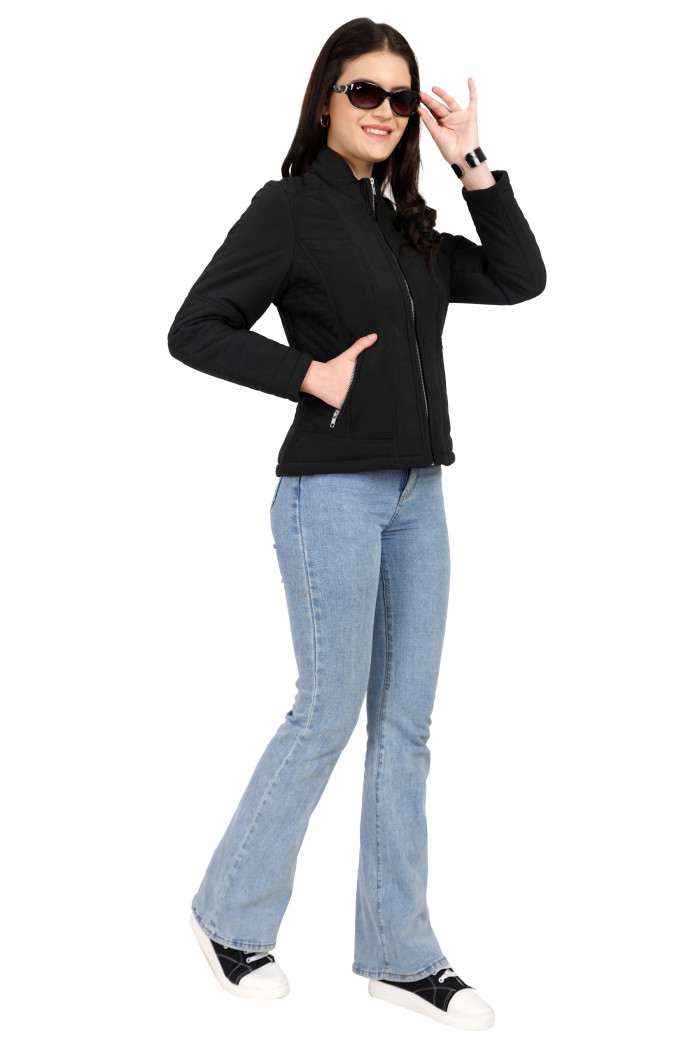 A woman in a standing pose, wearing Trufit’s black quilted biker jacket with a Chinese collar, sliver zip closure, and side pockets with a silver zipper and blue jeans, holding black shades with her left hand and right hand in pocket.