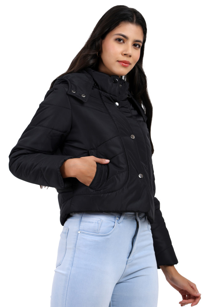 A woman in a standing side pose, wearing Trufit’s black quilted jacket with a high neck collar, zip closure, side pockets and blue jeans with her left hand in the pocket.