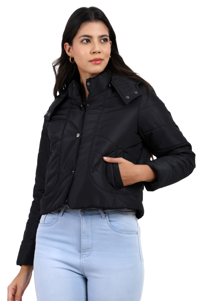 A woman in a standing side pose, wearing Trufit’s black quilted jacket with a high neck collar, zip closure, side pockets, blue jeans and holding the jacket’s collar with her right hand.