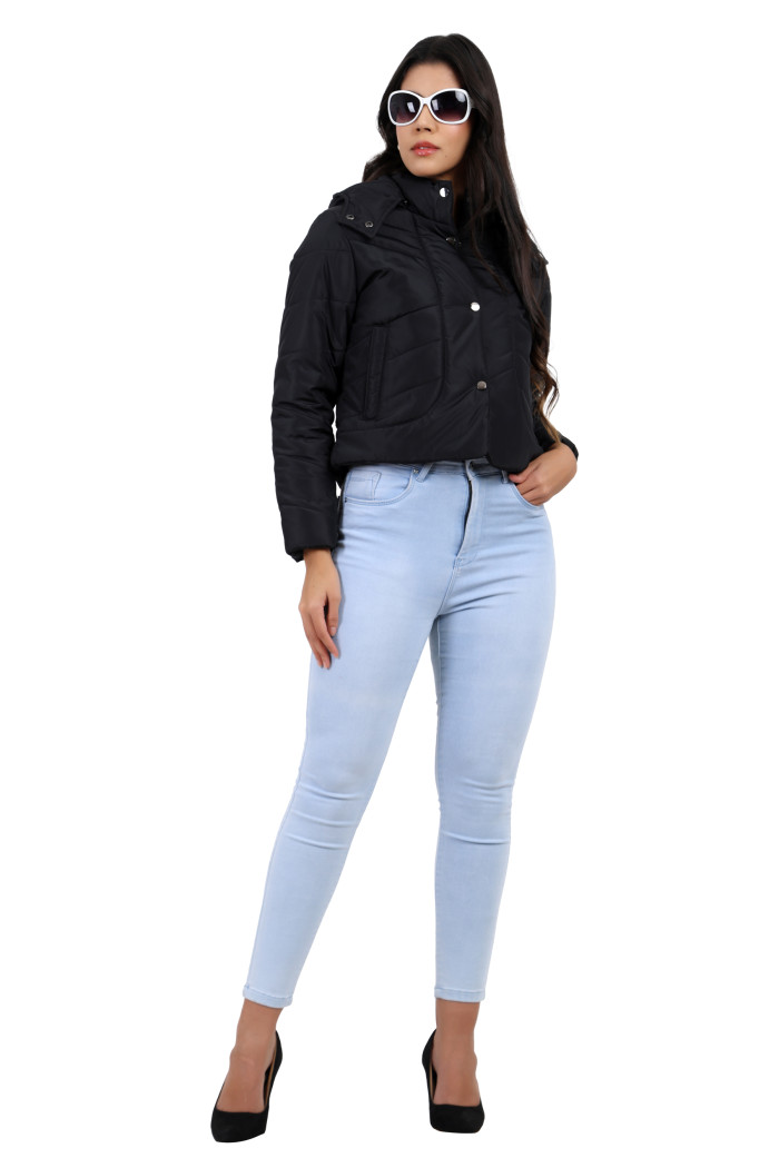 A woman in a standing pose in black shades, wearing Trufit’s black quilted jacket with a high neck, zip closure, side pockets, and blue jeans, is holding the jacket with her right hand.