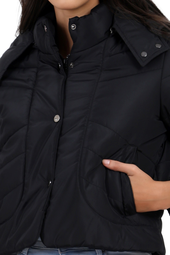 A cropped image of a woman wearing Trufit’s black quilted jacket with a high neck, zip closure, with both hands in her side pockets.