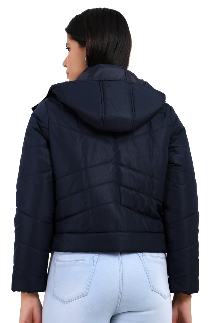 A back pose of a standing woman, wearing Coatsnmore’s navy quilted loose-fit crop jacket with a removable hood and quilted pattern.