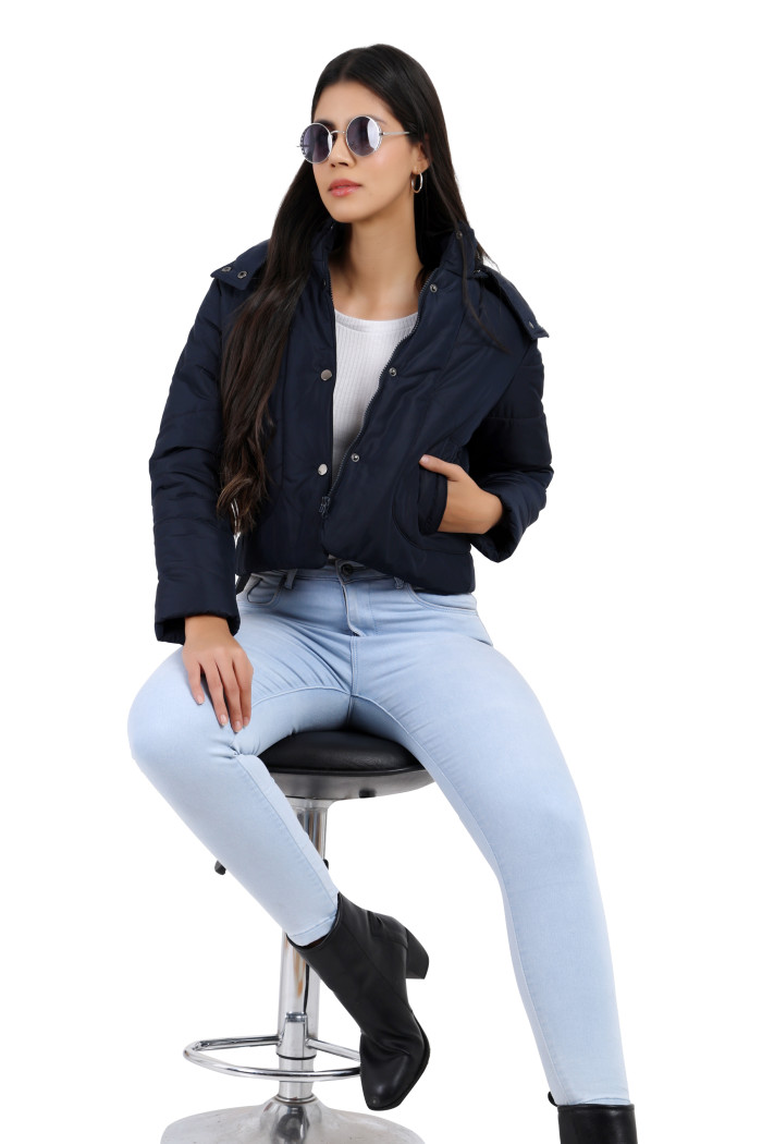 A woman in standing pose in black shades, wearing Coatsnmore’s black quilted loose-fit crop jacket featuring a Chinese collar, a removable hood, a zip closure with button closure, side pockets and blue jeans with one hand in the pocket.