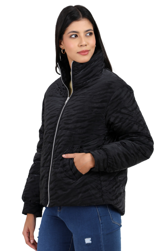 A woman in a standing side pose, wearing Trufit’s black quilted jacket with a high neck collar, zip closure, side pockets and blue jeans with her left hand in the pocket.