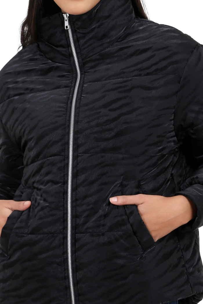 A cropped image of a woman wearing Trufit’s black quilted jacket with a high neck, zip closure, with both hands in her side pockets.