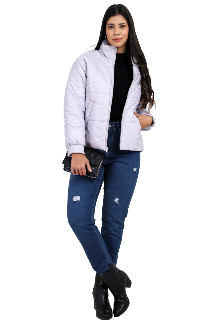 A woman in a standing pose, wearing Trufit’s mauve quilted jacket with a high neck, zip closure, side pockets, and blue jeans, is holding a clutch in her right hand and left hand in the pocket.