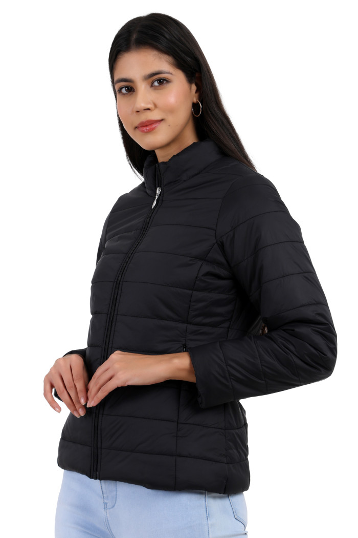 A woman in a side pose showcases the minimalist design of Coatsnmore’s black quilted jacket, complete with a high neck collar, zip-up front, side pockets, and blue jeans.