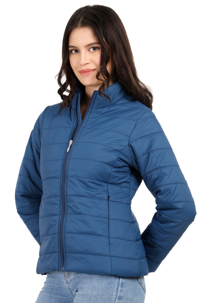 A woman in a side pose showcases the minimalist design of Coatsnmore’s blue quilted jacket, complete with a high neck collar, zip-up front, side pockets, and blue jeans.