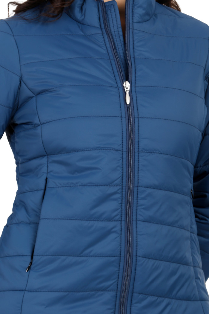 A cropped view of a woman in Coatsnmore’s blue quilted jacket, featuring a high neck collar, zip closure, and concealed zippered side pockets, with her right hand in the pocket.