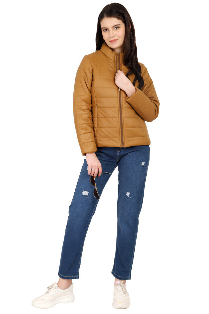 A woman in a standing pose, wearing Coatsnmore’s tan quilted jacket with a high neck, zip closure, side pockets, and blue jeans, is holding shades from her right hand and holding the jacket with her left hand.