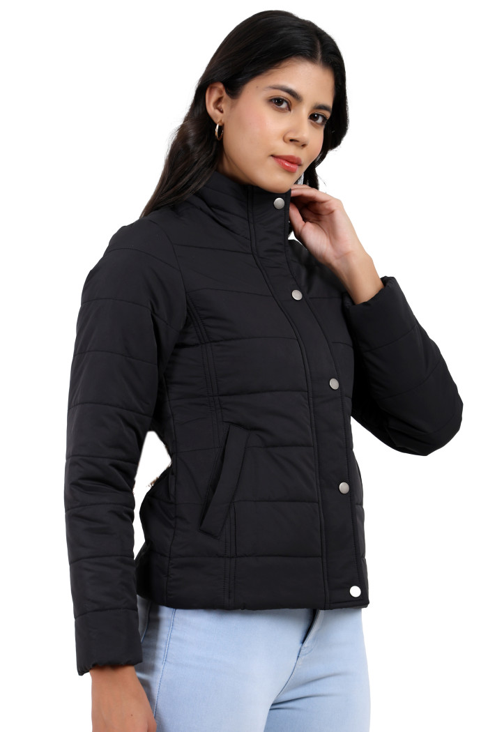 A woman in a standing pose, wearing Trufit’s olive quilted jacket without a hood with a high neck collar, zip closure, button placket, side pockets and blue jeans, with her hands in pockets.