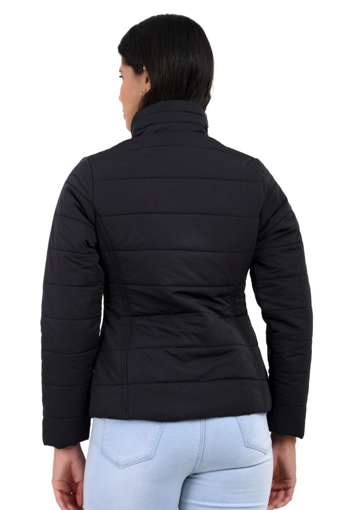 A back pose of a standing woman, wearing Trufit’s olive quilted jacket without a hood and blue jeans.