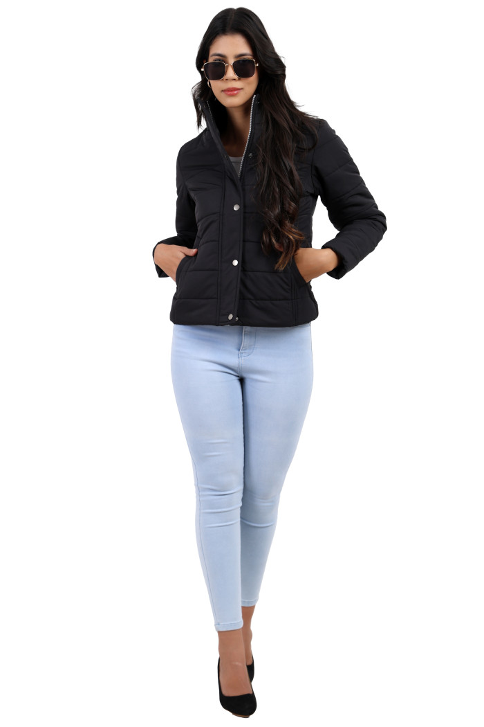 A woman in a sitting pose, wearing Trufit’s olive quilted jacket without a hood with a high neck, zip closure, button placket, side pockets, and blue jeans, while her right hand is in the pocket and holding the jacket with her left hand.