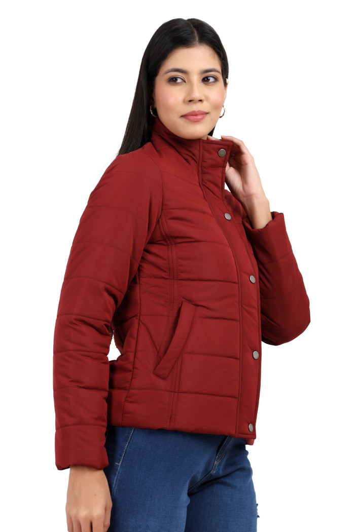 A side view of a woman highlights Coatsnmore’s navy quilted jacket, featuring a high neck collar, sleek zip closure, and concealed zippered side pockets, styled with blue jeans, holding the collar with her left hand.