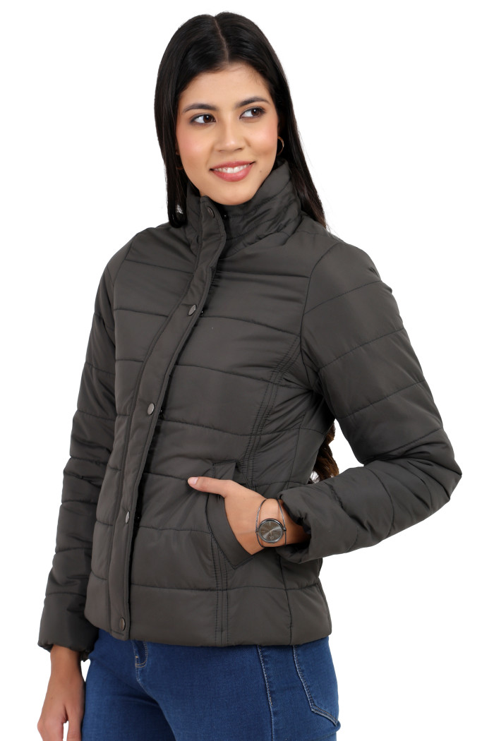 A woman in a standing side pose is wearing Trufit’s olive quilted jacket with a high neck collar, zip closure, button plackets, side pockets, and blue jeans while her left hand is in the pocket.