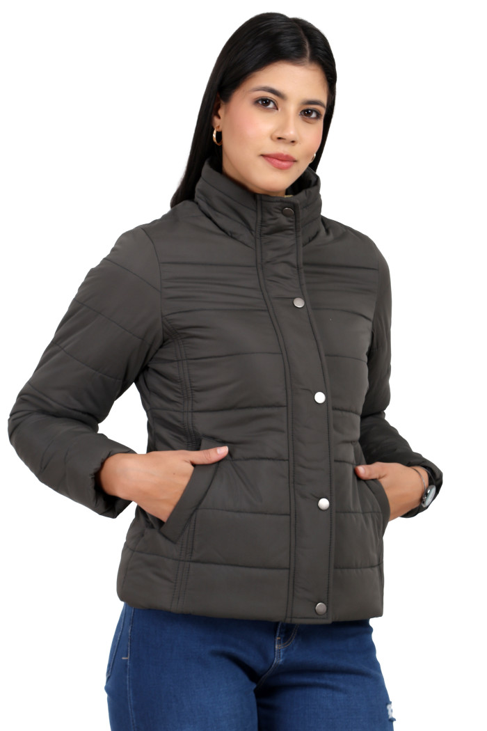 A woman in a standing pose, wearing Trufit’s olive quilted jacket without a hood with a high neck collar, zip closure, button placket, side pockets and blue jeans, with her hands in pockets.