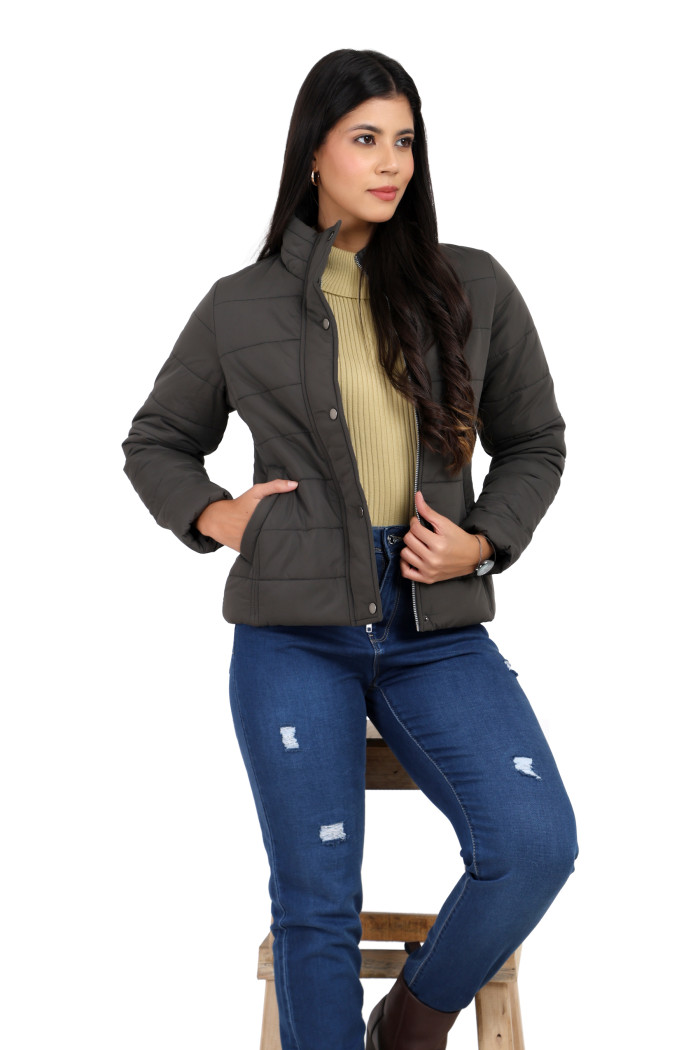 A woman in a sitting pose, wearing Trufit’s olive quilted jacket without a hood with a high neck, zip closure, button placket, side pockets, and blue jeans