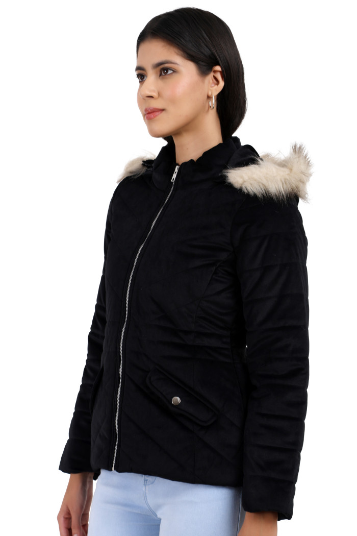 A woman in a standing side pose is wearing Trufit’s black velvet quilted jacket with a zip closure, removable hood with faux fur trim, high neck, slash pockets, and blue jeans.