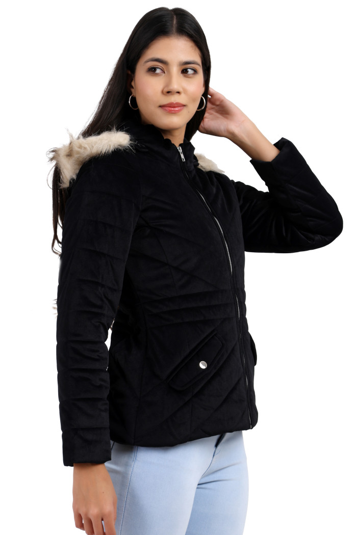 A woman is giving a side pose in a standing position, wearing Trufit’s black velvet quilted jacket with a zip closure, removable hood with faux fur trim, high neck, slash pockets and blue jeans.