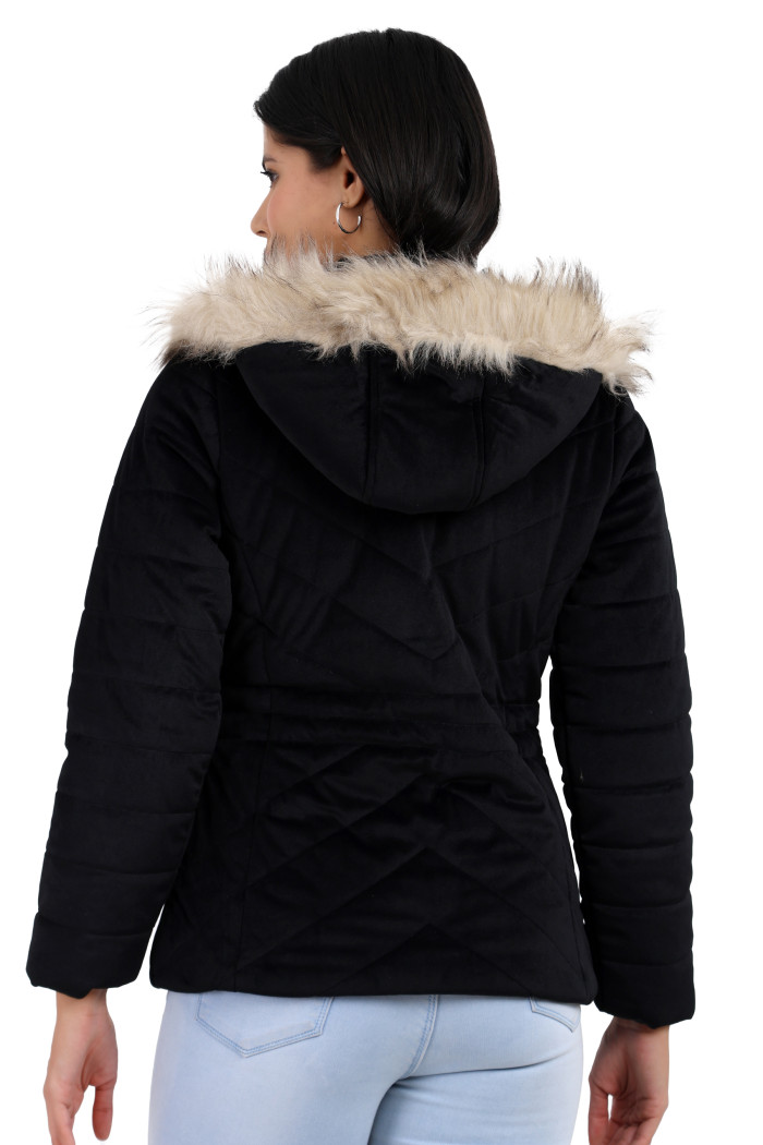 A back pose of a standing woman, wearing Trufit’s black velvet quilted jacket with a removable hood and blue jeans with her left hand on her head.