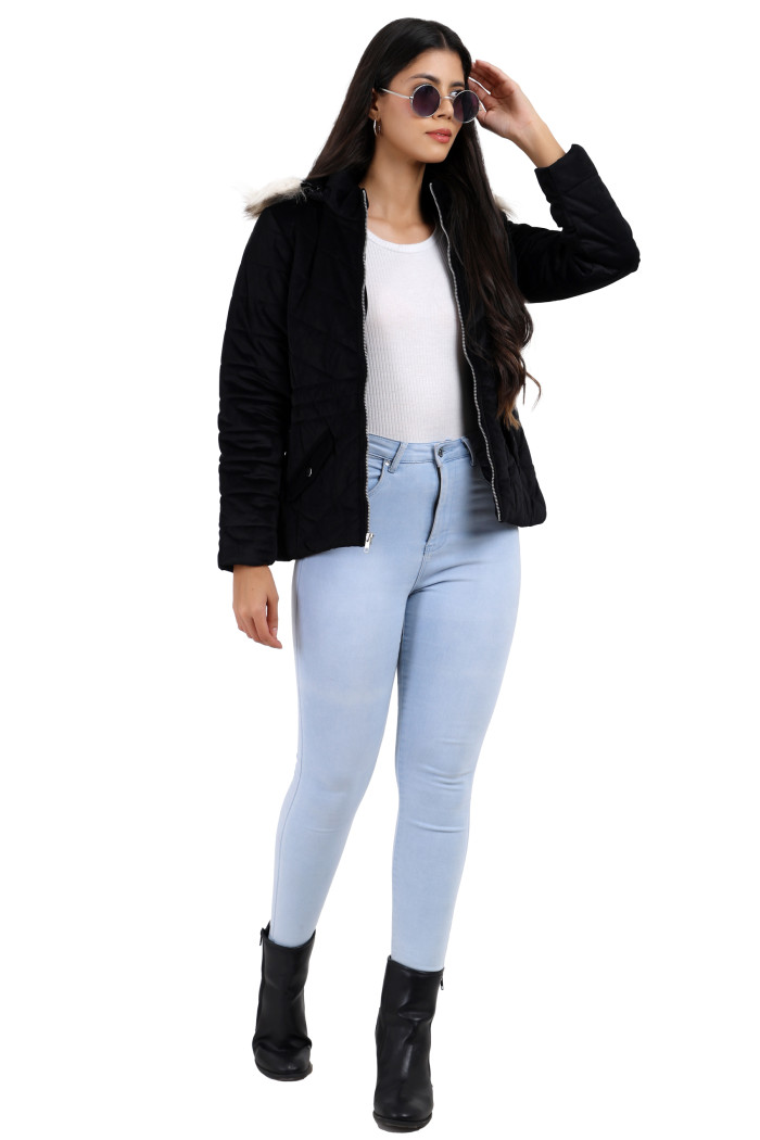 A woman is posing in a standing position in black shades, wearing Trufit’s black velvet quilted jacket with a zip closure, removable hood with faux fur trim, high neck, slash pockets, and blue jeans, while her left hand is on her head.